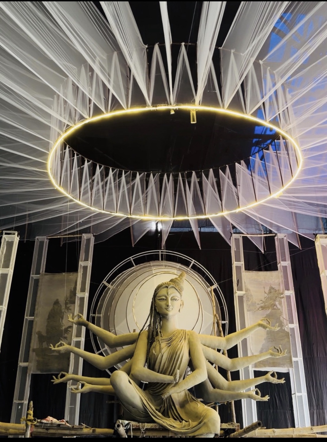 Wide shot of an ivory Durga idol seated beneath a vast spiked white canopy ringed in gold light